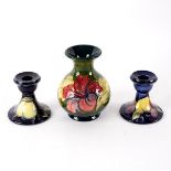 A Moorcroft Hibiscus pattern vase, 14cm high and a pair of Moorcroft Wisteria pattern candlesticks,