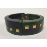 A Bakelite hinged black and green bangle with square brass inlays