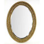 An oval wall mirror in decorative plaster gilt frame,