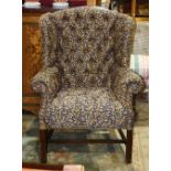 Georgian style wingback armchair, having royal blue and gold colored upholstery and rising on