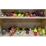 Two shelves of hardstone and glass fruits and vegetables including oranges, bananas, grapes,