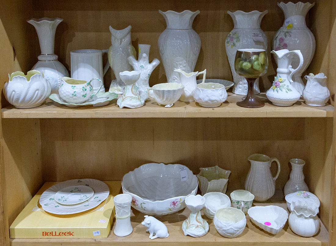 Two shelves of mostly Belleek table articles including vases, pitchers, etc., with various date