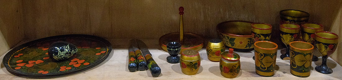 One shelf of Russian lacquer tableware including egg cups, a serving plate, utensils, etc.