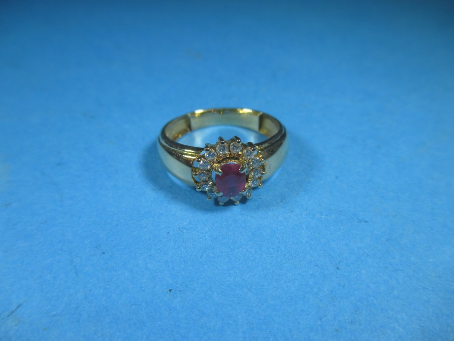 A yellow gold ring with central oval ruby surrounded by 14 brilliant cut diamo