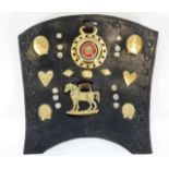 An antique leather shield with various horse brass