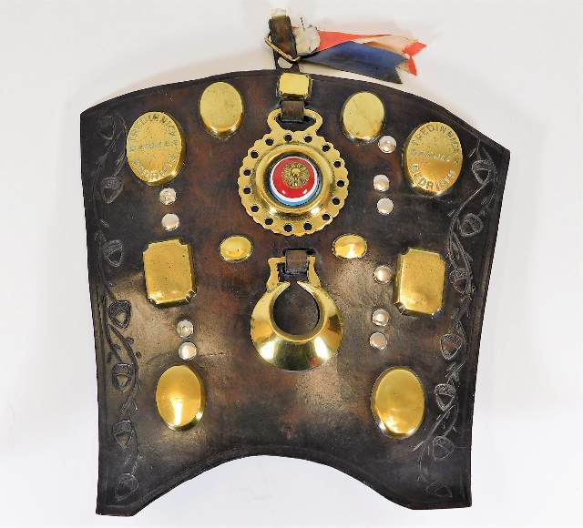 An antique leather shield with various horse brass