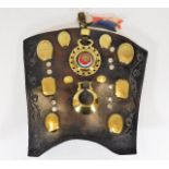 An antique leather shield with various horse brass