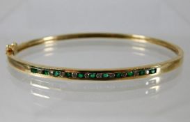 A 10ct gold bangle set with diamonds and emeralds