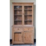 Stripped pine two stage cabinet having a glazed upper section enclosing three shelves, the lower