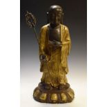 Oriental bronze and gilt bronze figure of a holy man holding a staff standing on an oval lotus