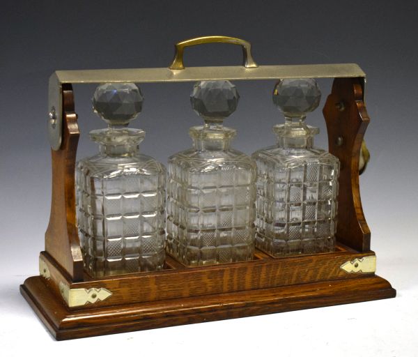 Edwardian oak three bottle tantalus of typical design with military dedication 'Presented to Col.