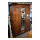 Victorian mahogany triple wardrobe with arch-panelled doors and mirror plate enclosing tray shelves,