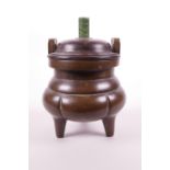 A Chinese bronze two handled censer of lobed form on tripod supports, with a turned hardwood cover