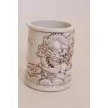 A Chinese white glazed ceramic brush pot with raised dragon decoration, impressed mark to base