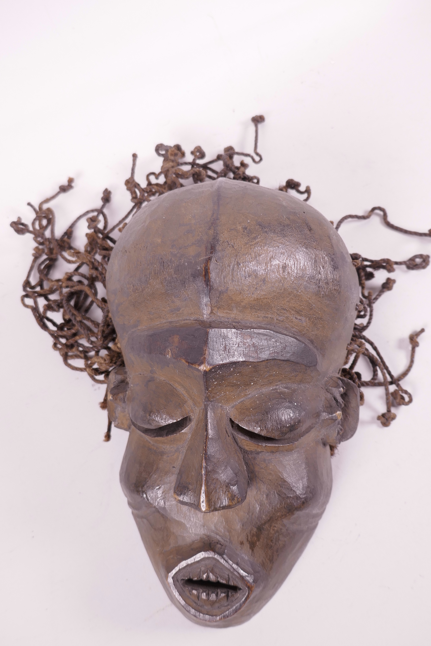An African carved wood tribal mask with string hair, (Ivory Coast), 9½" long