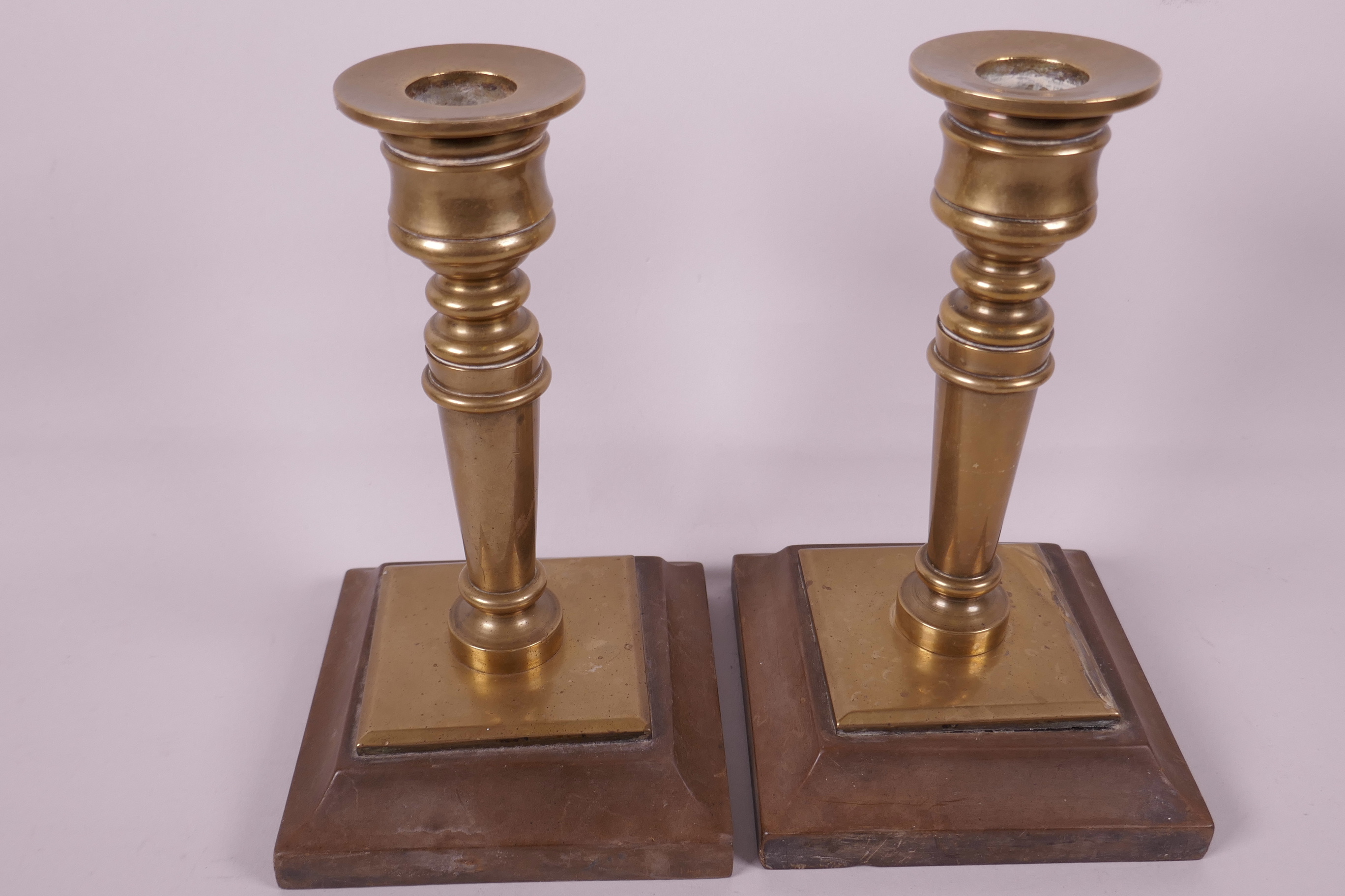 A pair of solid brass candlesticks on composition bases, 7" high