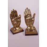 A pair of polished brass bookends cast as hands on square wooden bases, 8" high