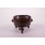 A Chinese patinated bronze censer of barrel form with two mask handles, raised on tripod feet in the