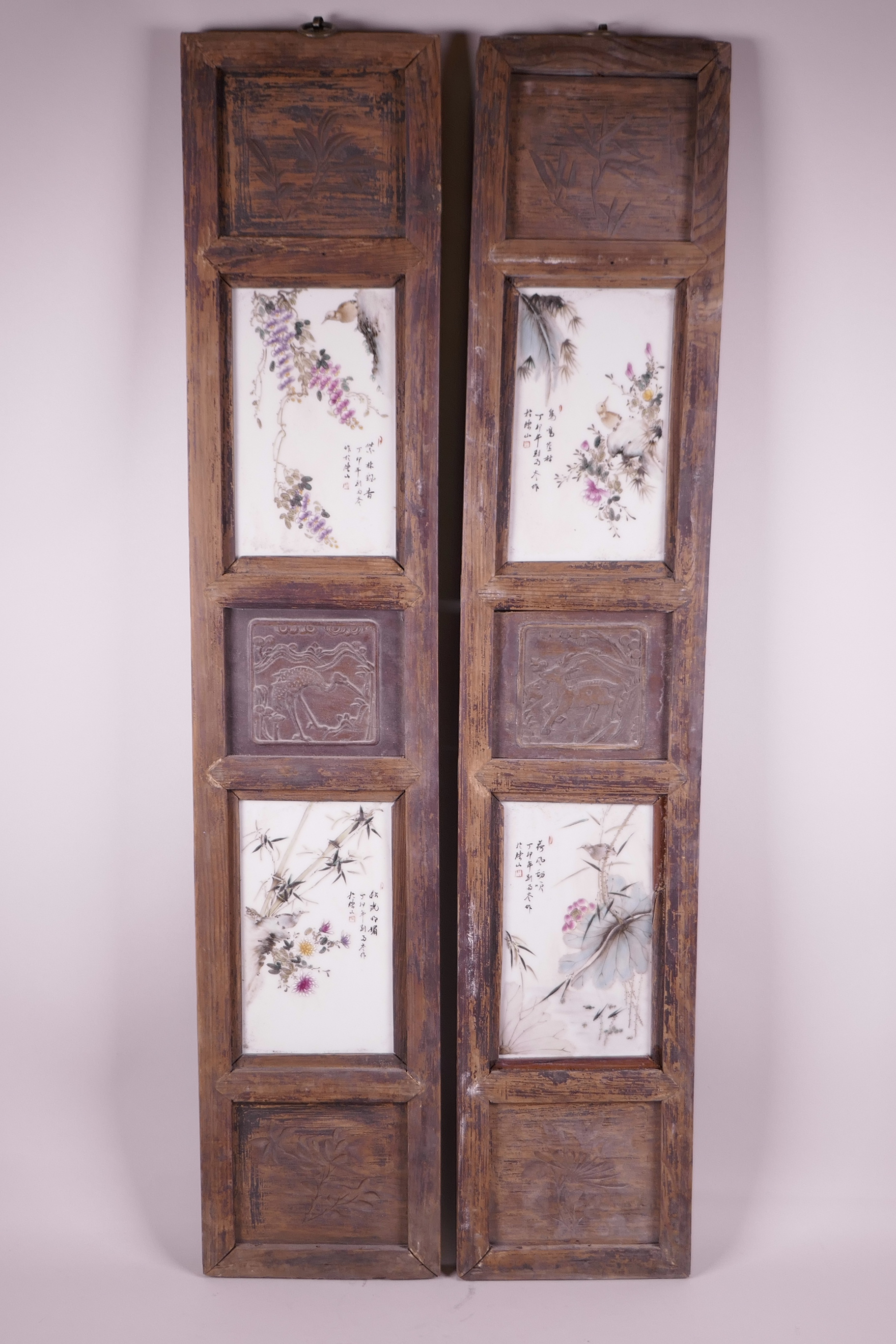 A pair of Chinese hardwood panels set with four polychrome enamelled porcelain panels depicting