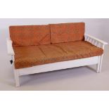 A mid C20th painted day bed with an extending sideways motion and orange upholstered cushions,