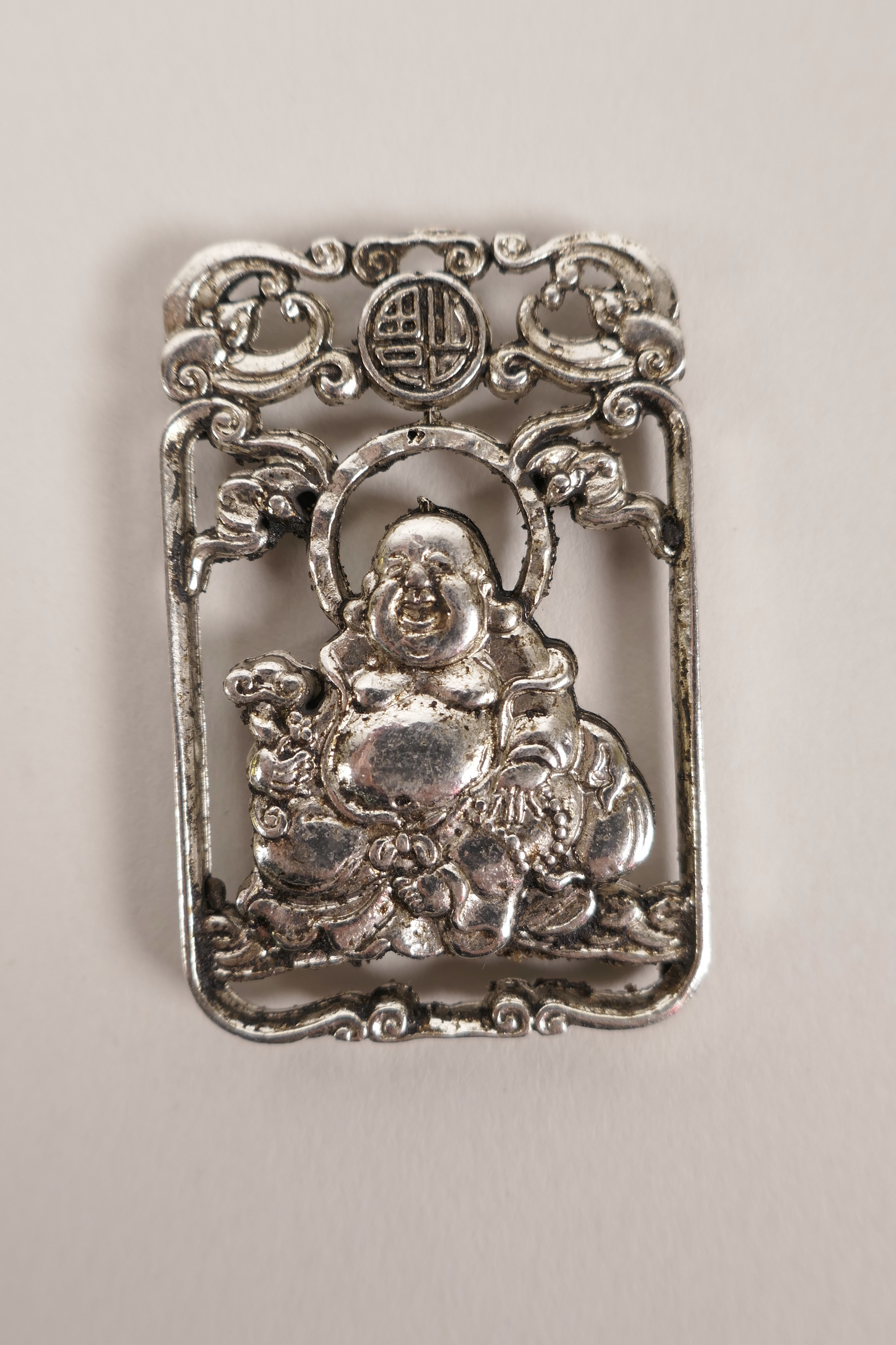 A Chinese silvered metal pendant decorated with a jolly Buddha, 2" x 1"