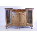 A 1930s walnut bowfronted display cabinet with central cupboards flanked by glazed doors, raised