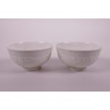 A pair of Chinese celadon glazed porcelain tea bowls with raised scrolling floral decoration to