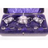 A cased three piece silver plated table cruet of two salts and a mustard pot with blue glass liners,