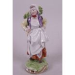 A porcelain figurine of a Dutch girl carrying a basket of vegetables on her back, painted in