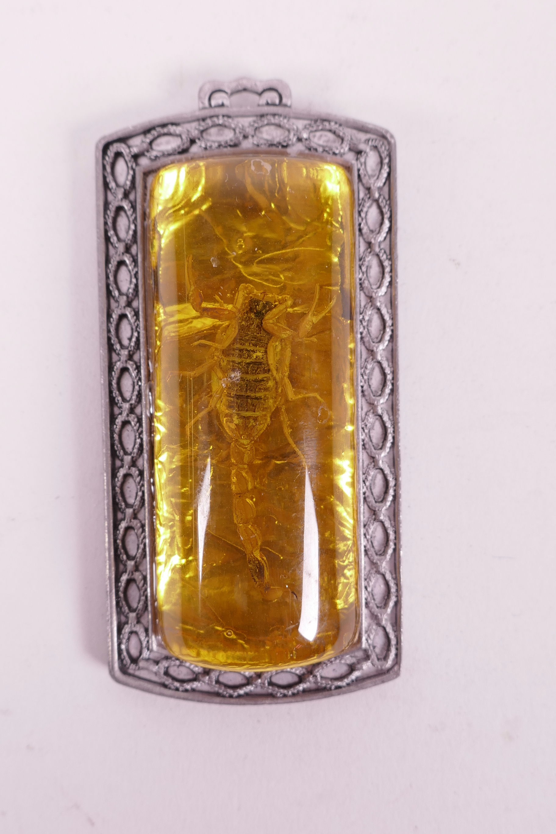 A Chinese silvered metal pendant set with a piece of faux amber containing a scorpion, 3½" long