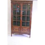 A Continental oak two door display cabinet with carved frieze and classical swag decoration, 40" x