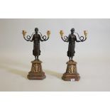 A pair of bronze and ormolu two branch Empire style candelabra in the form of heralds, mounted on
