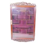 A Chinese hardwood wall mounted trinket disply cabinet with single glazed door, carved crest and