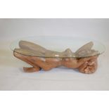 A carved wood occasional table in the form of a reclining nude, with bevelled glass top, 27" x 51" x