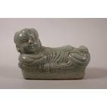 A Chinese celadon glazed pottery pillow in the form of a child, impressed mark to base, 8" wide
