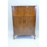 An Art Deco figured walnut serpentine fronted cupboard, with sunburst veneered decoration, the two