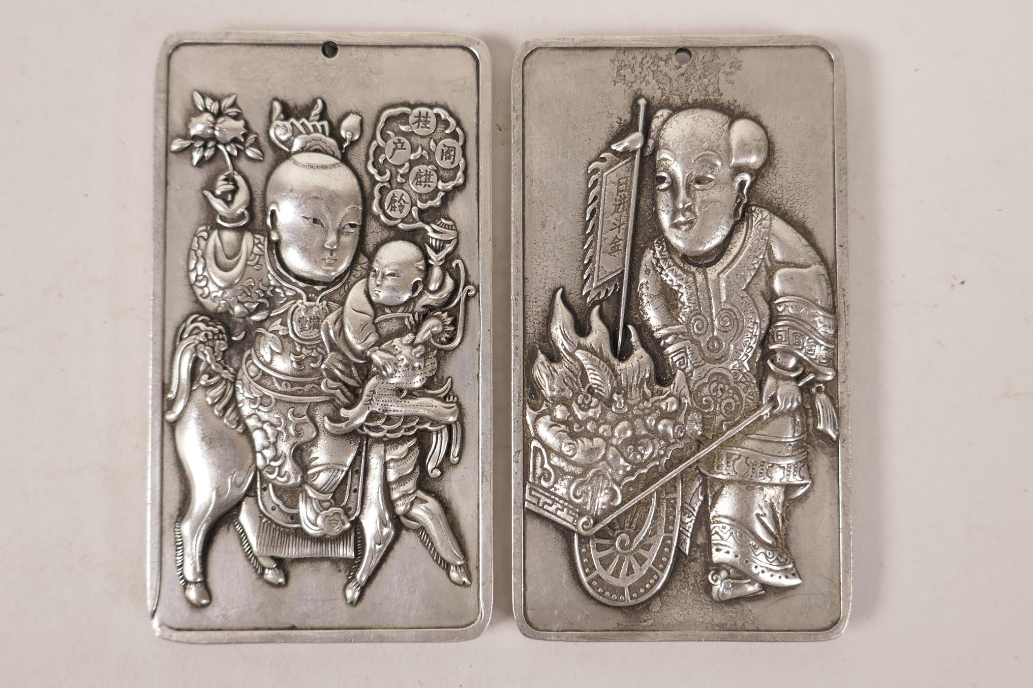 A pair of Chinese white metal scroll weights decorated with a 'figure and cart' and children