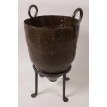 A riveted metal urn with two ring handles on a wrought iron stand, 13"high