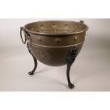 A brass cauldron on three cast iron legs, 13" high, 14" diameter