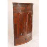 An early C19th figured mahogany bowfronted hanging corner cupboard, with two arched panel doors over