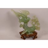 A Chinese carved green jade figurine of two birds on a flowering branch, 7" high, on a carved wooden
