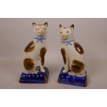 A pair of Staffordshire pottery figurines of cats seated on blue cushions, 7½" high