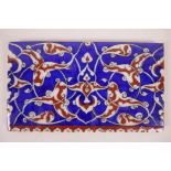 A Turkish Kutahya pottery tile with stylised decoration in a blue and red palette, 8" x 5"