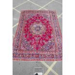 A large Persian Mashad carpet with a traditional central floral medallion on a red field, within a