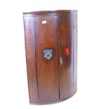 An early C19th elm bowfronted two door hanging cupboard, painted with heraldic shields, 24" x 37"