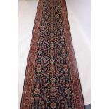 A Persian hand knotted wool runner with red borders and stylised floral pattern on a deep blue