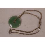 A Chinese green jade pi disc pendant on a leather necklace with white metal decoration and clasp