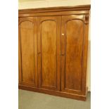 A Victorian mahogany wardrobe with three arched doors and carved corbels, fitted with slides,