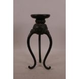 A Chinese bronze stand on tripod supports with dragon mask decoration, 9½" high