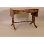 A Regency style yew wood sofa table on lyre end supports and brass cap castors, with two true and
